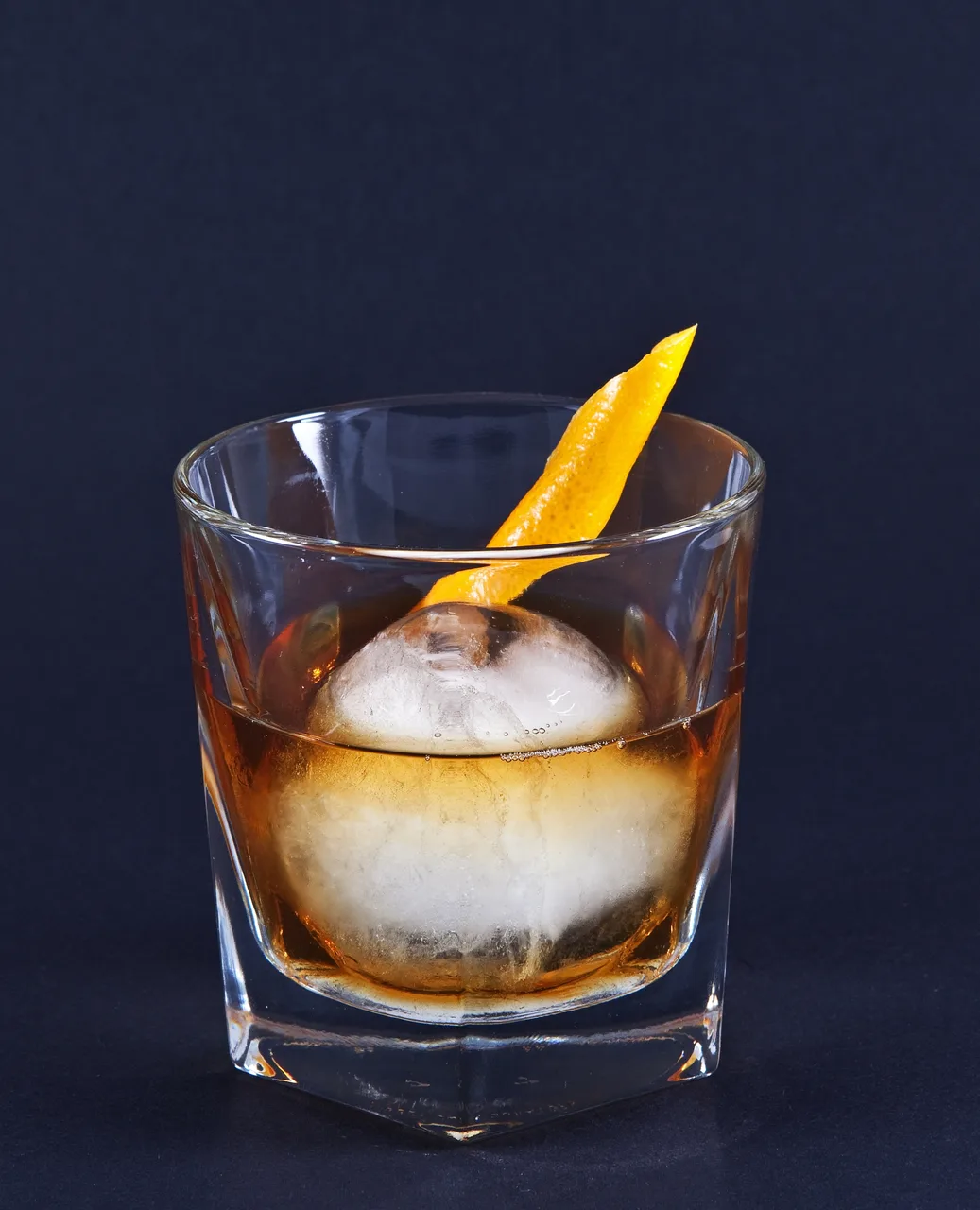 Old Fashioned servido em copo baixo com cubo de gelo grande e casca de laranja torcida